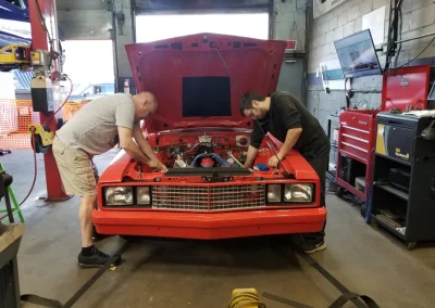 Team working under the hood of Orange Ford Fairmont 1 Team working under the hood of Orange Ford Fairmont